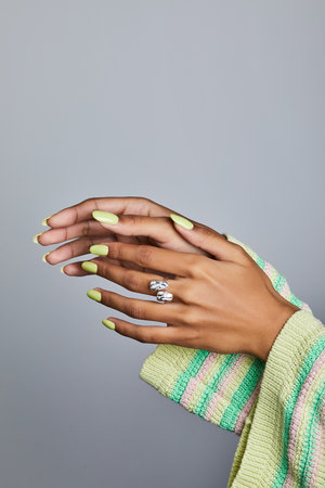Stylish female hand with lime-green manicure and silver ring emerging from a pastel striped knit sleeve on gray backgroundの写真素材