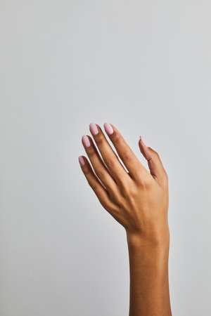 Womanâs hand with soft pink manicure against a neutral grey background, showcasing smooth skin and elegant nail finishの写真素材
