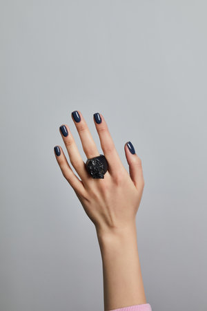 Elegant hand with navy manicure and bold black statement ring against a clean gray studio backgroundの写真素材