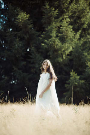 Beautiful girl laughs and dances outdoors in meadow during sunsetの写真素材