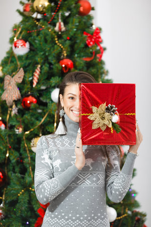 Beautiful happy young woman with gifts by the New Year treeの写真素材