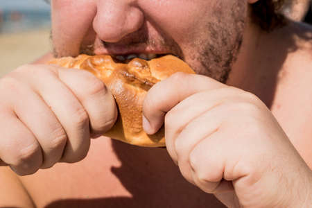Fat man on the beach eating a pieの写真素材
