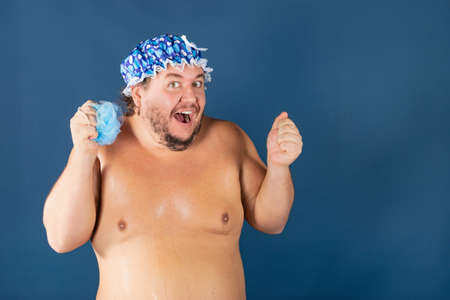 Funny fat man in blue cap and with sponge in the shower. Fun and cleanlinessの写真素材
