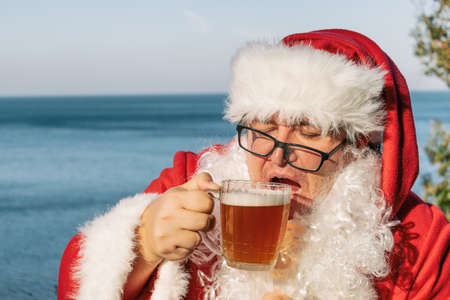 Fat man dressed as Santa drinking beer on the oceanの写真素材