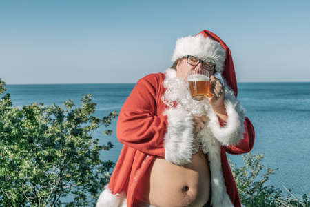 Fat man dressed as Santa drinking beer on the oceanの写真素材