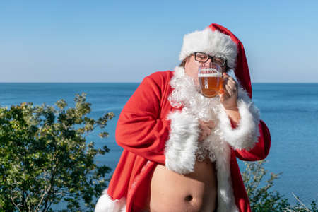 Fat man dressed as Santa drinking beer on the oceanの写真素材