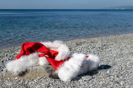 Santa Claus clothing and hat lies on a large stone on the seashoreの写真素材
