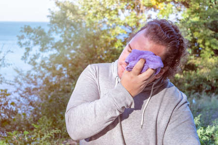 Fat man wipes his face with a towel standing on the ocean