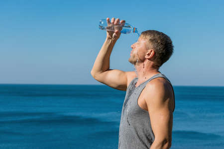 A man pours water on his face from a plastic bottle on the oceanの写真素材