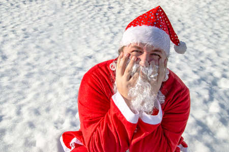 Funny fat man dressed as santa claus is sitting on the snowの写真素材