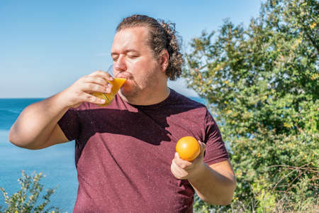 Funny fat man on the ocean drinking juice and eating fruitsの写真素材