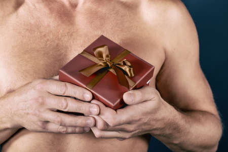 Shirtless man holds a gift box isolated on white. Surprise. Holiday and special occasion.の写真素材
