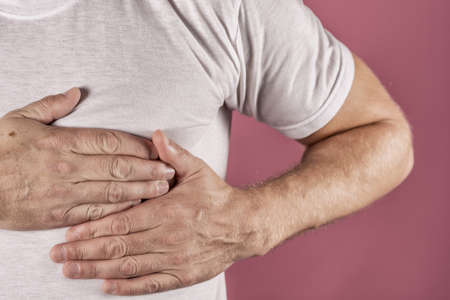 Severe heartache, man suffering from chest pain, having heart attack or painful cramps, pressing on chest with painful expression.の写真素材