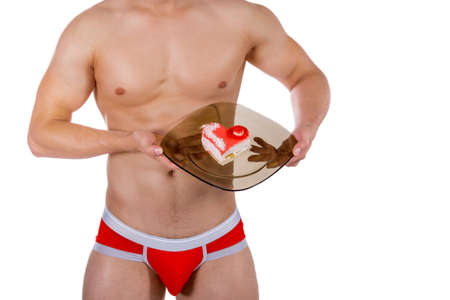Torso of young handsome guy with heart-shaped cake on a plate. Sexy portrait of romantic man with valentineの写真素材