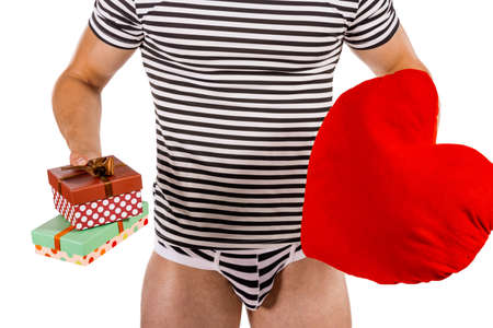Torso of young handsome guy with heart pillow and gift boxes. Sexy portrait of romantic man with valentineの写真素材