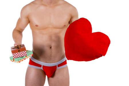 Torso of young handsome guy with heart pillow and gift boxes. Sexy portrait of romantic man with valentineの写真素材