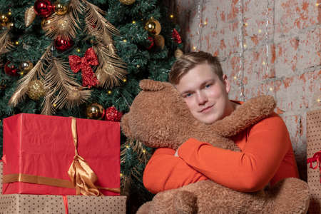 Handsome guy hugs the bear sitting under the tree surrounded by giftsの写真素材