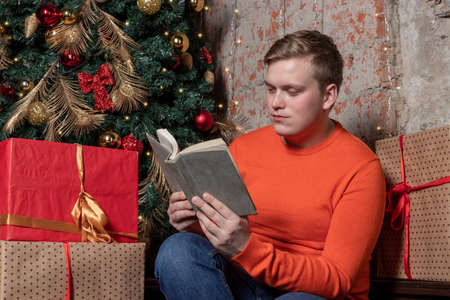 Handsome guy is reading a book sitting under the tree surrounded by giftsの写真素材