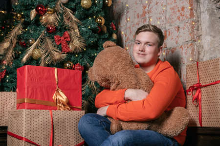 Handsome guy hugs the bear sitting under the tree surrounded by giftsの写真素材