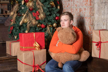 Handsome guy hugs the bear sitting under the tree surrounded by giftsの写真素材