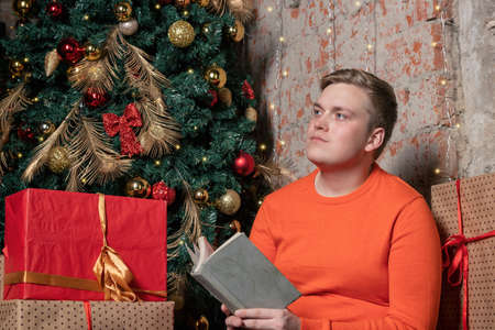 Handsome guy is reading a book sitting under the tree surrounded by giftsの写真素材