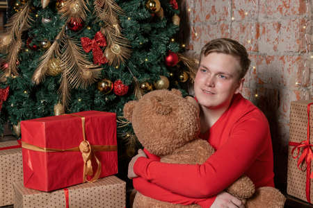 Handsome guy hugs the bear sitting under the tree surrounded by giftsの写真素材