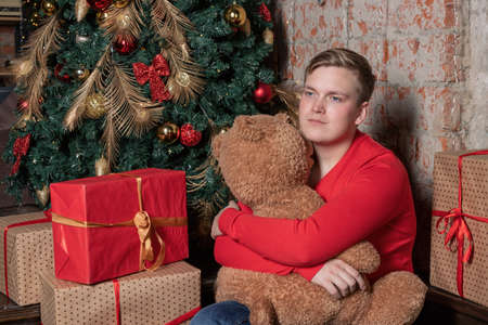 Handsome guy hugs the bear sitting under the tree surrounded by giftsの写真素材
