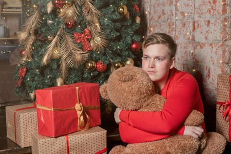 Handsome guy hugs the bear sitting under the tree surrounded by giftsの写真素材