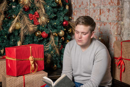 Handsome guy is reading a book sitting under the tree surrounded by giftsの写真素材