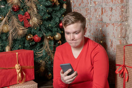 Handsome guy chatting on the new phone sitting under the tree surrounded by boxes of giftsの写真素材