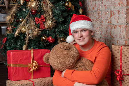 Handsome guy hugs the bear sitting under the tree surrounded by giftsの写真素材