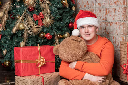 Handsome guy hugs the bear sitting under the tree surrounded by giftsの写真素材