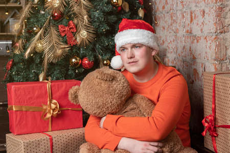 Handsome guy hugs the bear sitting under the tree surrounded by giftsの写真素材