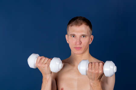 Closeup of a muscular young man lifting dumbbells on blue background