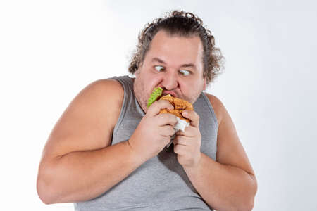 Portrait of funny fat man eating fast food burger isolatedの写真素材