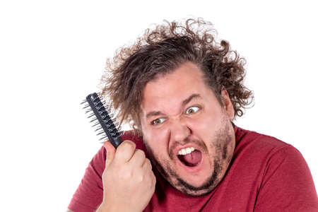Close up portrait of fat man tries to comb his tangled and naughty hair with a small black comb isolatedの写真素材