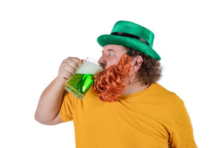 A smiling happy fat man in a leprechaun hat with green beer. He celebrates St. Patrickの写真素材