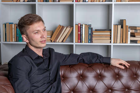 Handsome man sitting on couch by bookshelvesの写真素材
