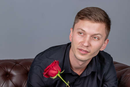 Handsome man wearing black shirt sitting on the leather sofa holding a roseの写真素材