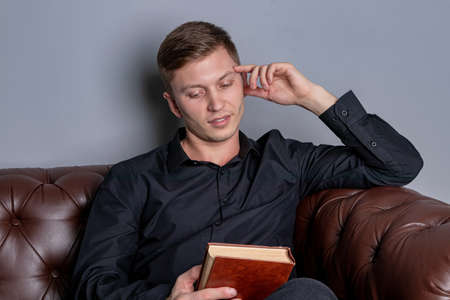 Young man is sitting on a sofa and reading a book