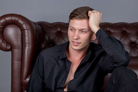 Sexy handsome man wearing black shirt sitting on floor near the leather sofaの写真素材