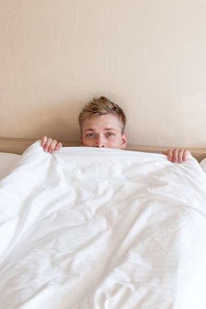 Funny guy in bed under the blanket after sleepingの写真素材