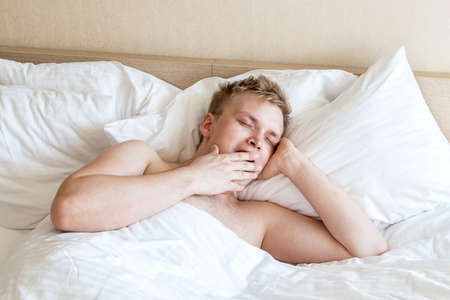 Funny guy in bed under the blanket after sleeping