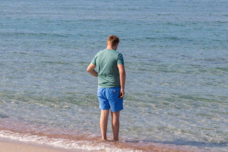 Young man in a t-shirt on the seashore and looks at the seaの写真素材