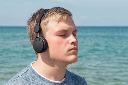 Portrait of a young man on the beach listening to music on headphonesの写真素材