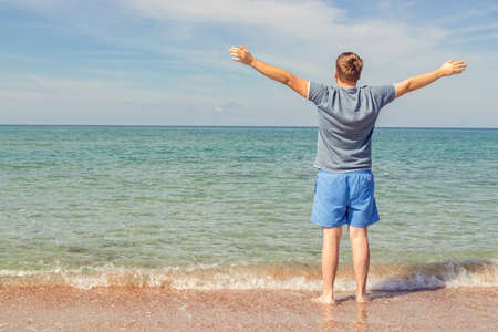 Young man in a t-shirt on the seashore and looks at the seaの写真素材