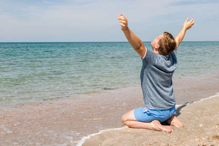 Young man in a t-shirt on the seashore and looks at the seaの写真素材