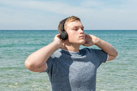 Portrait of a young man on the beach listening to music on headphonesの写真素材