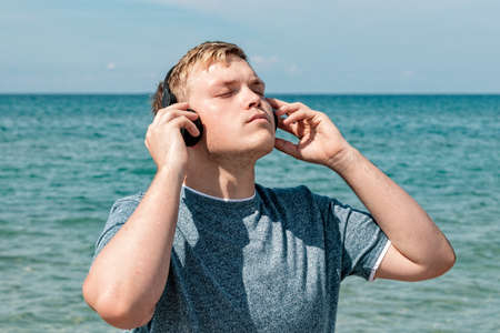 Portrait of a young man on the beach listening to music on headphonesの写真素材