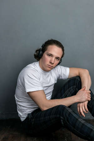 Handsome young man sitting on the floor in living room, having headphones on his headの写真素材